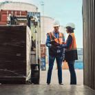 „Pracownicy logistyki w kamizelkach odblaskowych sprawdzają dokumenty przy załadunku palety do kontenera transportowego.