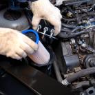 Dłonie w białych rękawiczkach wkładają jasny wkład filtra do pionowej obudowy w silniku wysokoprężnym.