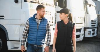 Menadżer floty i kobieta spacerujący obok ciężarówek, rozmawiając ze sobą.