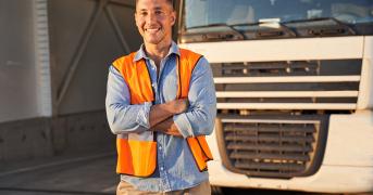 Uśmiechający się kierowca ciężarówki, który stoi przed pojazdem.