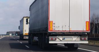 Dwie duże ciężarówki z naczepami typu plandeka jadące drogą szybkiego ruchu.