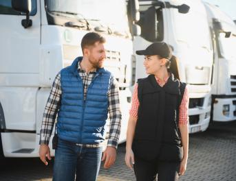 Menadżer floty i kobieta spacerujący obok ciężarówek, rozmawiając ze sobą.