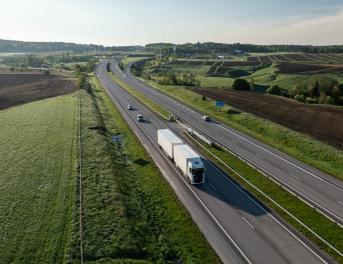 Ciężarówka na drodze wśród wschodzącego słońca i zielonych krajobrazów.