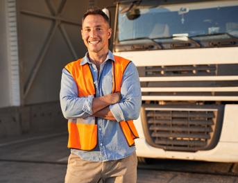 Uśmiechający się kierowca ciężarówki, który stoi przed pojazdem.