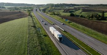 Ciężarówka na drodze wśród wschodzącego słońca i zielonych krajobrazów.