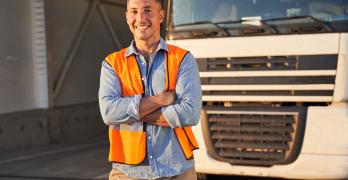 Uśmiechający się kierowca ciężarówki, który stoi przed pojazdem.