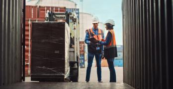 „Pracownicy logistyki w kamizelkach odblaskowych sprawdzają dokumenty przy załadunku palety do kontenera transportowego.