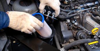 Dłonie w białych rękawiczkach wkładają jasny wkład filtra do pionowej obudowy w silniku wysokoprężnym.