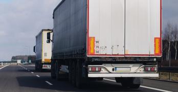 Dwie duże ciężarówki z naczepami typu plandeka jadące drogą szybkiego ruchu.